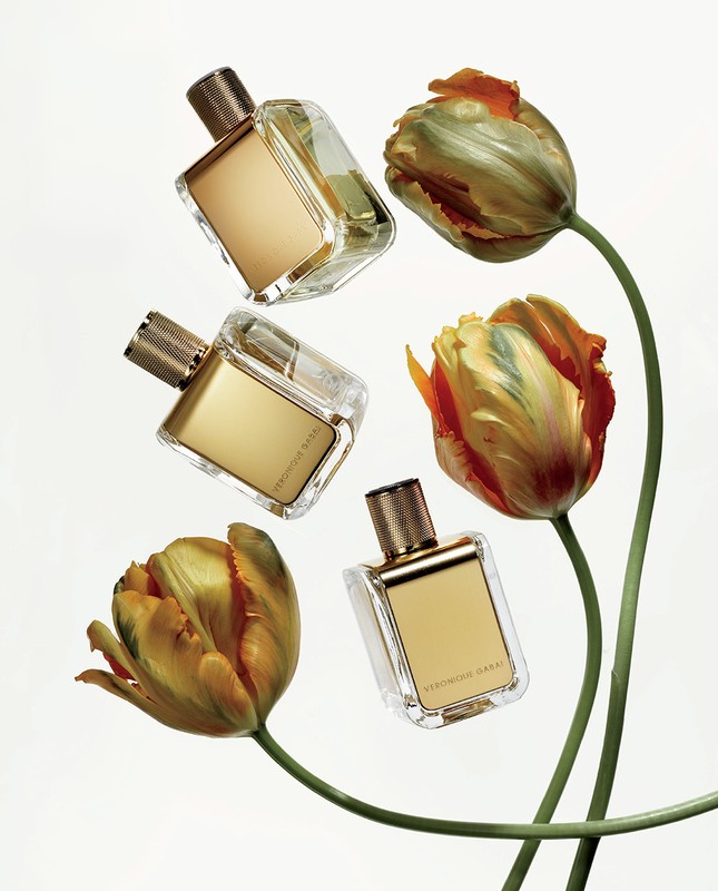Still life studio shot: three perfume bottles with gold caps and accents paired with orange and green tulips, against white.