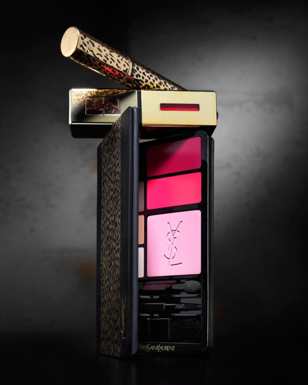 Luxury makeup kit with a palette of pink and red shades, gold lipstick and eyeliner with animal print, studio shot on dark background.