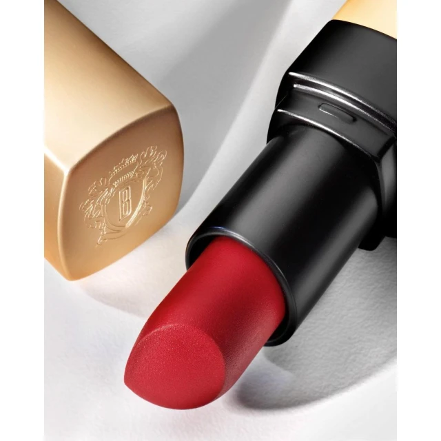 Close-up of a red lipstick tube with a gold cap alongside its separate gold lid on a white surface, showcasing beauty product.