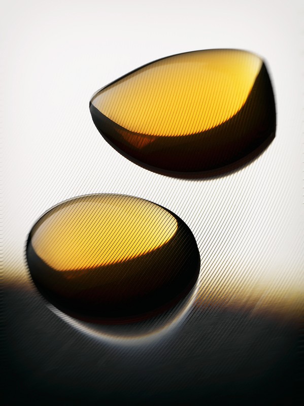 Two translucent amber gel capsules rest on a textured white surface, creating a minimalist, abstract still life with subtle light gradients.