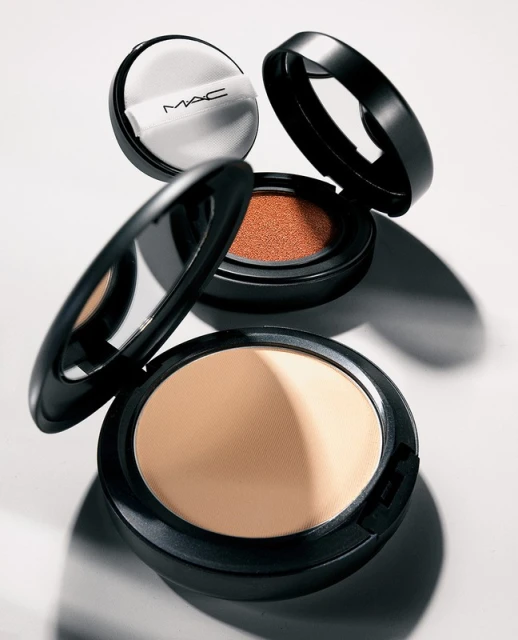 Makeup powder compacts with black cases and light-colored powder, on a white surface. Beauty and cosmetics product photography.