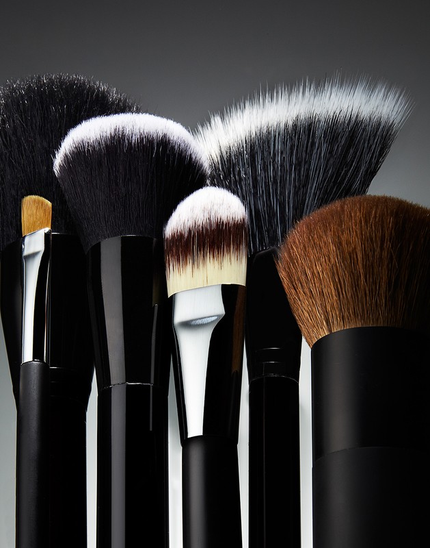 Macro studio shot displaying a collection of professional makeup brushes with black handles and varying head sizes and bristle colors.
