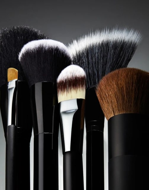 Macro studio shot displaying a collection of professional makeup brushes with black handles and varying head sizes and bristle colors.