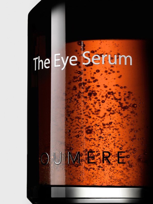 A close-up of OUMERE The Eye Serum bottle reveals its rich, amber-hued liquid formulation against a neutral backdrop, highlighting its premium skincare presentation.