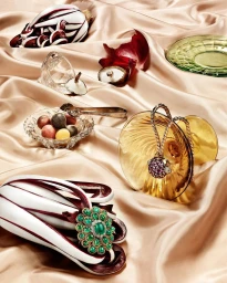 An ornate emerald brooch resting on a white and purple radicchio head over a glossy champagne silk fabric backdrop.