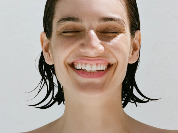 Close-up portrait of smiling woman with wet dark hair and natural makeup against a plain white background