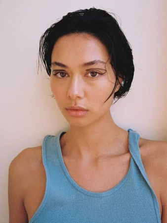 Close-up portrait of a woman with short dark hair and graphic eyeliner wearing a blue ribbed tank top.