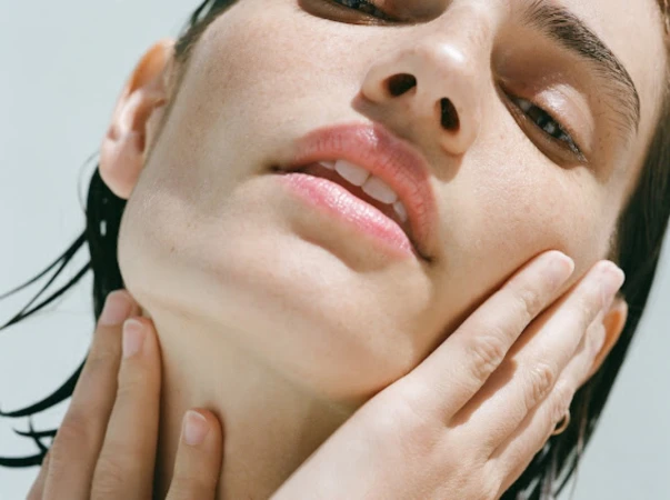 Close-up beauty portrait of a woman with wet hair touching her jawline and neck, featuring natural makeup.