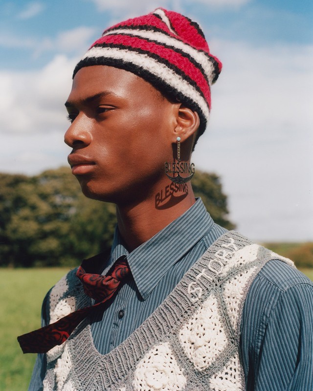 Close-up of a young man with a knit hat and statement earring outdoors in a field, showcasing fashion and portrait photography.