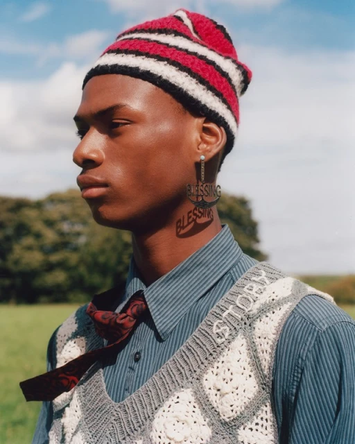 Close-up of a young man with a knit hat and statement earring outdoors in a field, showcasing fashion and portrait photography.