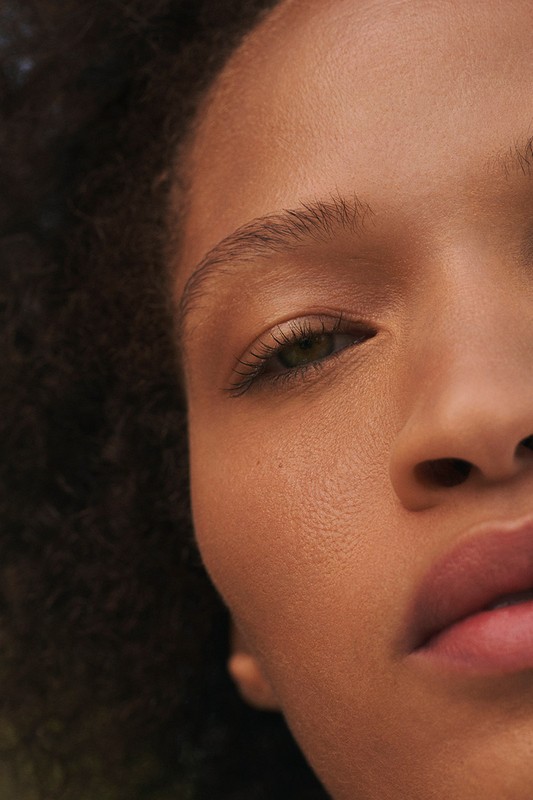 Close-up portrait showcasing the face of an adult female with curly dark hair and smooth skin. The image emphasizes the woman's facial features.