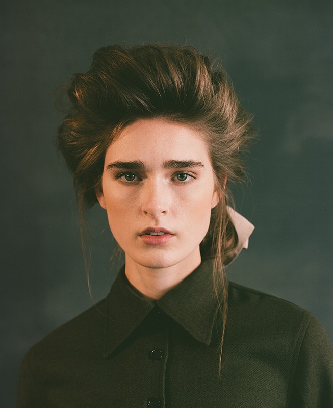 Portrait of a woman with voluminous styled brown hair wearing a dark green collared button-down shirt.