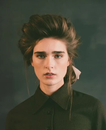 Portrait of a woman with voluminous styled brown hair wearing a dark green collared button-down shirt.