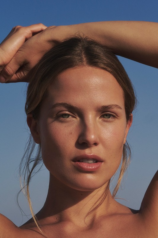 Close-up beauty portrait of a woman with her arms raised against a clear blue sky background.