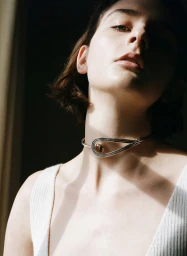 Close-up portrait of a woman wearing a silver choker necklace and white ribbed top under dramatic light