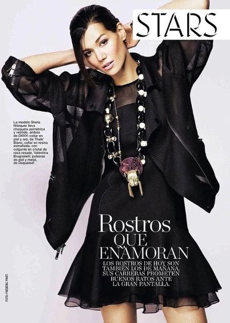 Editorial fashion shot of a woman wearing a black dress and a large pendant necklace, posing with her hands up near her head.