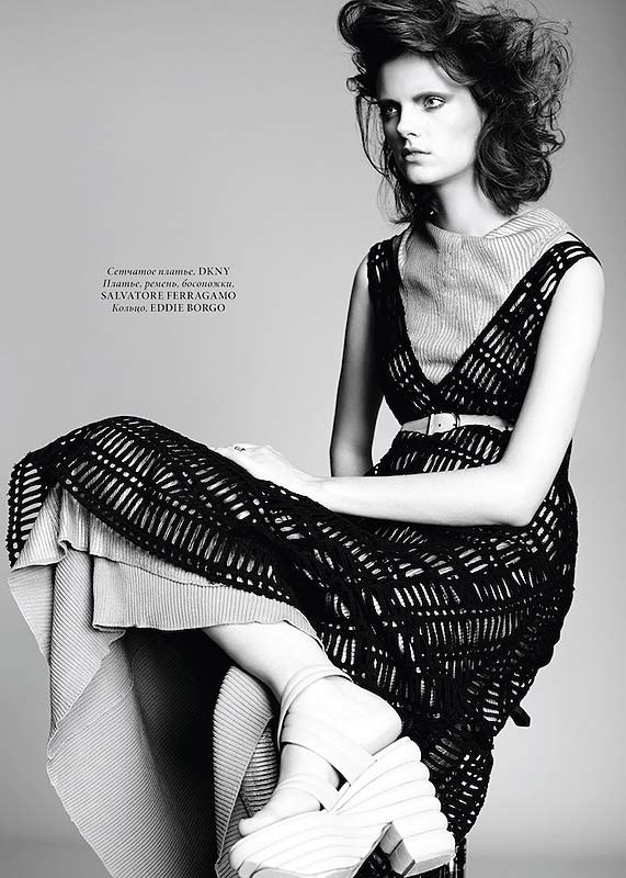 Model seated in a black knit dress with platform shoes against a grey background