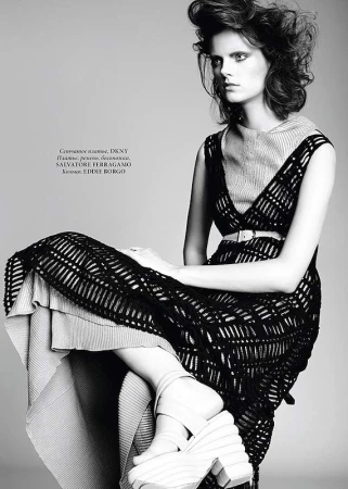 Model seated in a black knit dress with platform shoes against a grey background