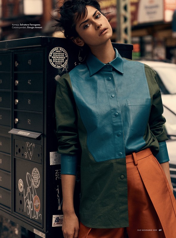 Fashion shot of a woman posing near a mailbox in a city street, wearing a color-blocked button-down shirt and high-waisted skirt.