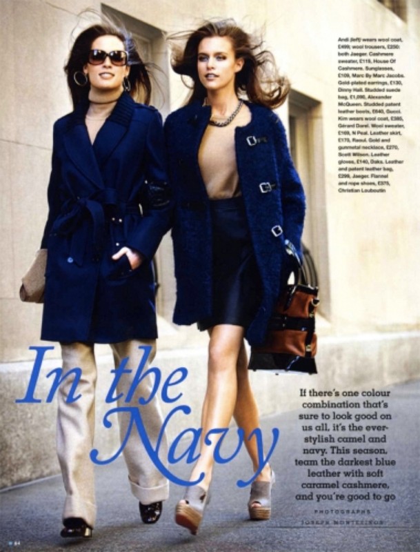 Two women model navy blue coats in a fashion editorial. The blonde woman carries a brown handbag and wears platform heels.