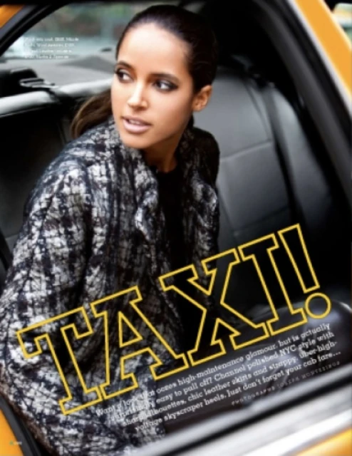 Fashion editorial shot of an adult woman in a textured coat sitting inside a yellow taxi cab looking out the window, natural daylight.