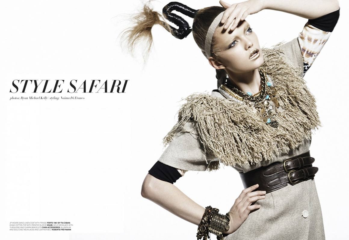 Fashion editorial shot of a woman with a unique updo wearing a gray coat, layered necklaces, an ornate bracelet, and statement makeup.