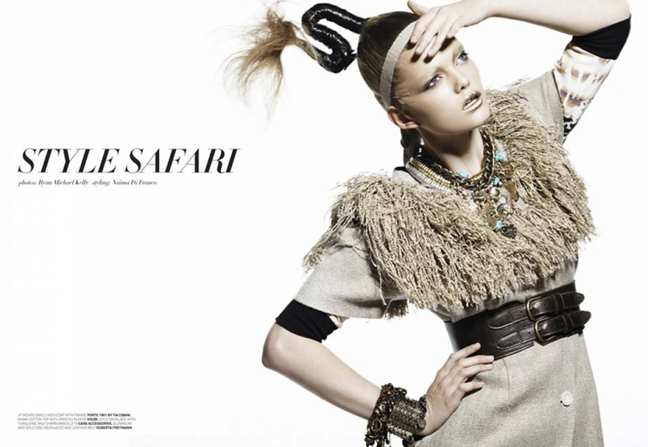 Fashion editorial shot of a woman with a unique updo wearing a gray coat, layered necklaces, an ornate bracelet, and statement makeup.