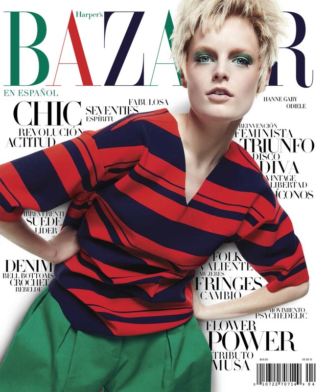 Fashion magazine cover featuring a model with short blonde hair, wearing a striped shirt and green pants, posing against a white backdrop.