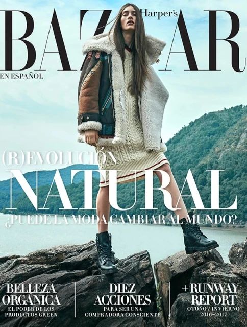 Bazaar En Espanol cover featuring a female model in a sweater dress, shearling jacket, and boots, standing on rocks with a water and mountain background.