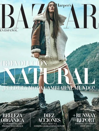 Bazaar En Espanol cover featuring a female model in a sweater dress, shearling jacket, and boots, standing on rocks with a water and mountain background.