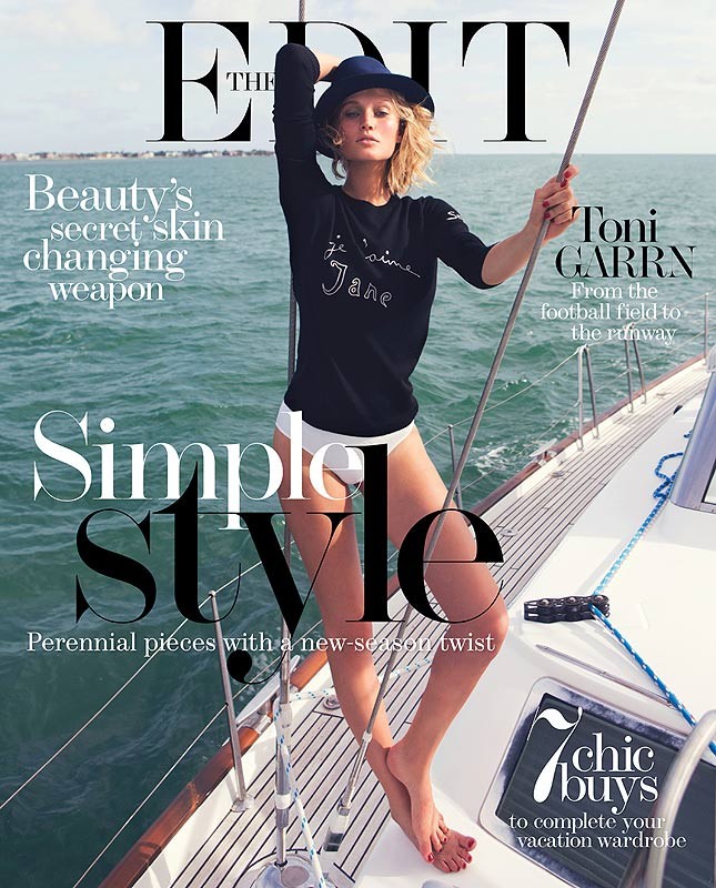 Fashion editorial cover of Toni Garrn on sailboat. Model wears navy sweater, white bottoms, and hat, set against ocean backdrop.