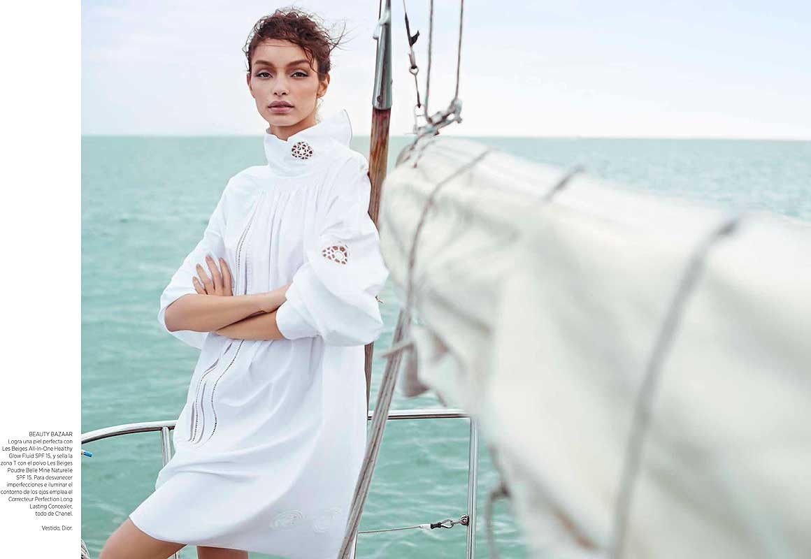 Fashion shot of woman in white dress on yacht, ocean backdrop, embodying nautical editorial style and showcasing effortless chic.