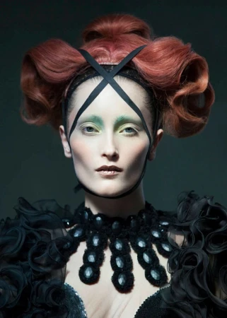Portrait of a woman with an elaborate auburn hairstyle, black headdress, and decorative black collar, against a dark gray backdrop.