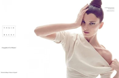 Model with high top knot hairstyle and winged eyeliner wearing an off-shoulder cream top against a bright white background