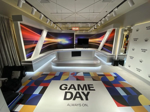Well-lit television studio setup with graphic walls, geometric floor pattern, and console, ready for broadcast, empty of people.