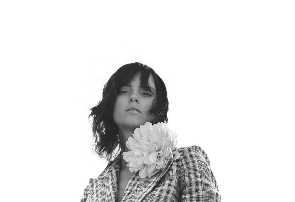 Monochrome portrait of a woman with dark hair in a patterned blazer with a large white flower, against a bright white background.
