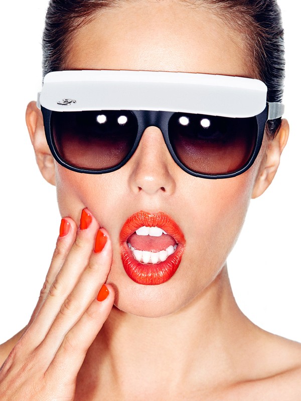 Glamorous woman with surprised expression wears novelty sunglasses and bright lipstick, posing on a white background.