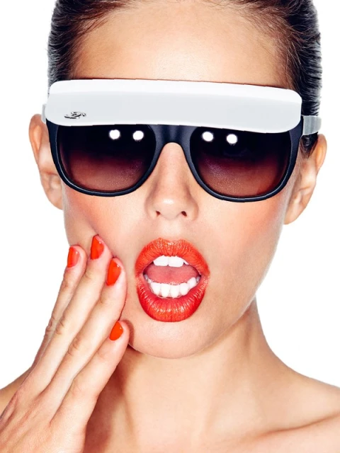 Glamorous woman with surprised expression wears novelty sunglasses and bright lipstick, posing on a white background.