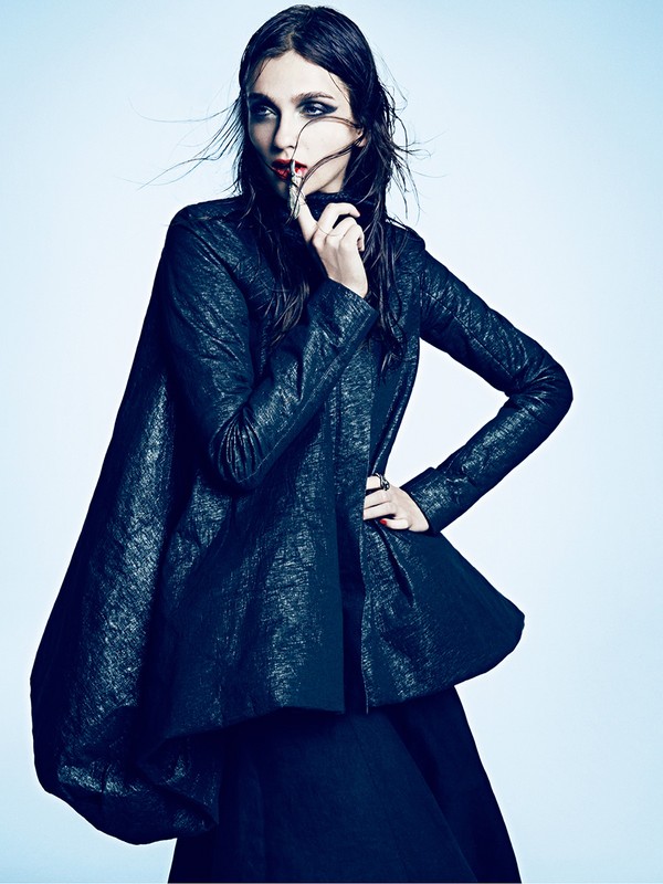 Elegant woman poses in black high-fashion outfit with dramatic makeup in a photo studio with soft lighting. Fashion, beauty, and editorial.