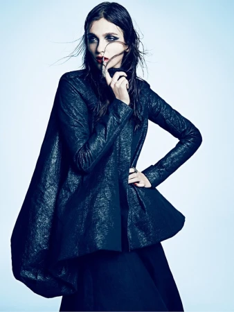 Elegant woman poses in black high-fashion outfit with dramatic makeup in a photo studio with soft lighting. Fashion, beauty, and editorial.