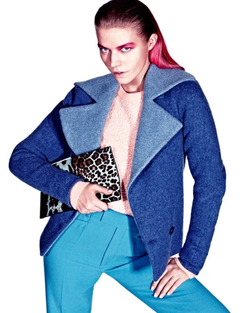 Fashionable woman in blue coat and pants holding a leopard print clutch, posing in a studio with pink eyeshadow and hair.