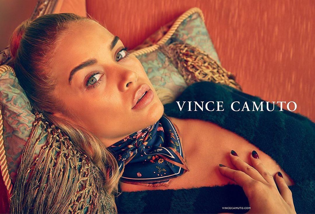Close-up fashion shot of a blonde woman lying on a patterned cushion, wearing a printed scarf, with VINCE CAMUTO text overlay.