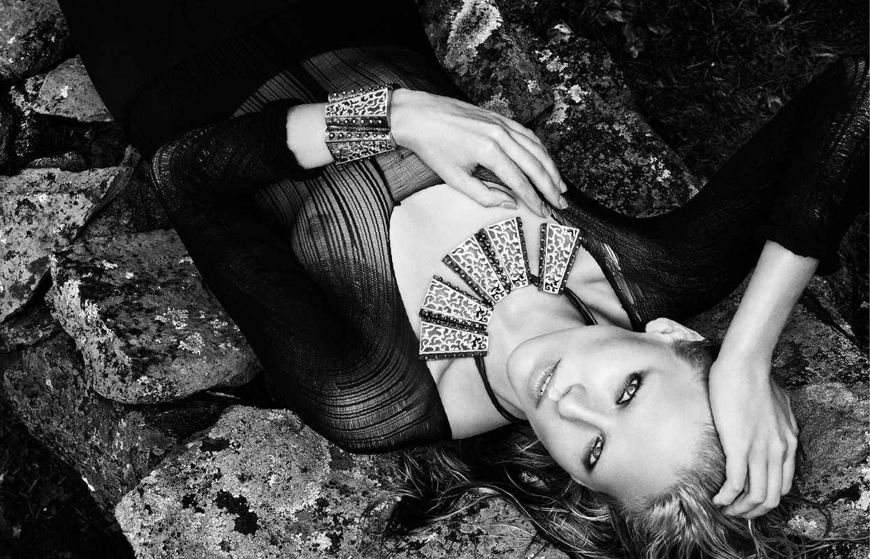 Black and white fashion shot of a woman lying on rocks wearing statement jewellery, including a necklace and matching cuff bracelet.