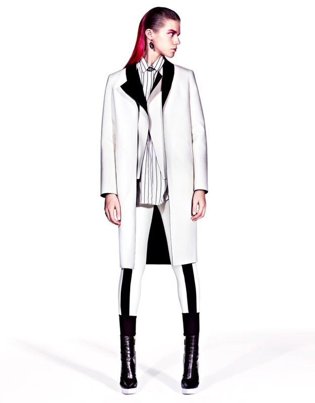 Fashion model in a stark white coat with black accents, paired with striped shirt and white leggings, in a studio setting, high contrast.