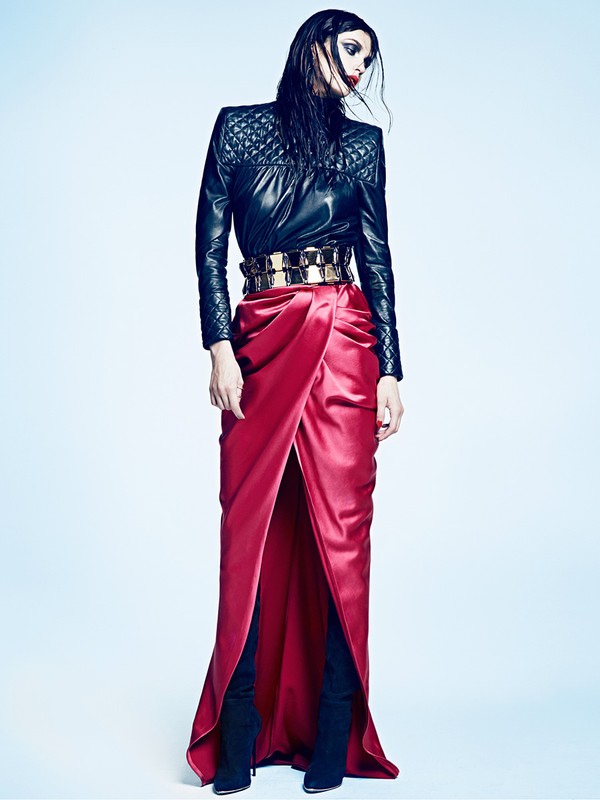 Model in quilted black leather top and red satin maxi skirt with gold belt against a blue gradient background