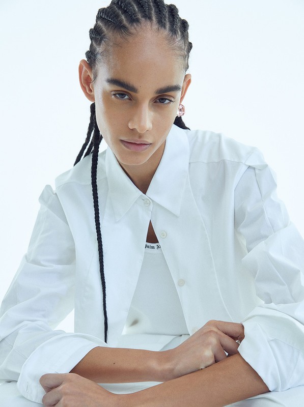Model in white collared shirt with braided hair posing against a clean white backdrop by James Macari.