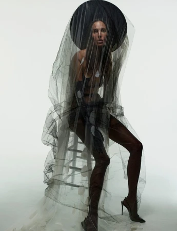 Model seated on a ladder wearing a sheer black veil and wide hat by photographer James Macari