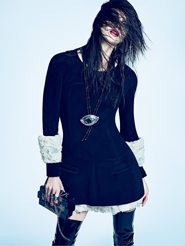 Fashion photo of an adult woman in a short black dress with white lace, wet hair over face, holding a small black box bag, and wearing boots.