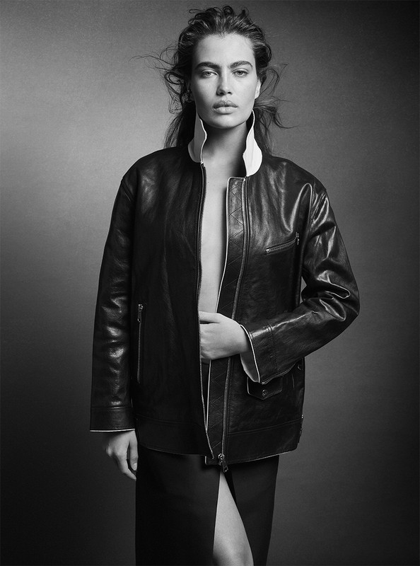 Monochrome portrait of a woman wearing a dark leather bomber jacket with a tall collar against a plain studio background.