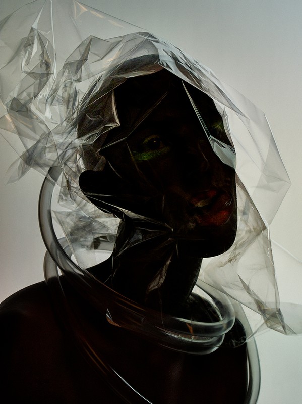 Person encased in transparent plastic and tubes against a light background. Dark skin and facial expression are partially visible.
